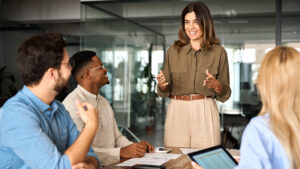 Happy middle aged business woman executive ceo leader discussing project management planning strategy working with diverse colleagues company team