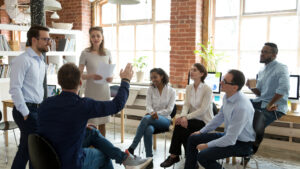 Ambitious male employee raise hand ask question to female presenter at meeting