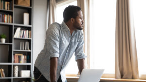 businessman leaning on table with laptop, looking away